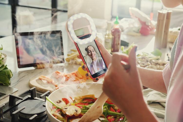 Ragazza che cucina e tiene in mano un dispositivo MediaWorld.